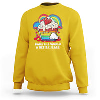 Yellow sweatshirt with colorful rainbow baker graphic and “Bake the World” text