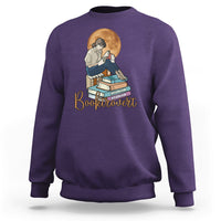 Purple women’s sweatshirt with front “Booktrovert” graphic of reader and stacked books