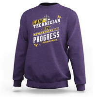 Purple crewneck sweatshirt with filmstrip "In Progress" graphic and scales icon