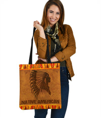 Brown tote bag with black headdress print, orange tribal border, and black shoulder straps