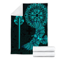 Folded black blanket with teal Viking raven tattoo art; rolled white blanket beside