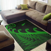 Green area rug laid on floor with fern fronds and koru shapes; dark geometric pattern.