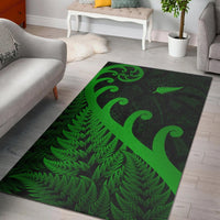 Green area rug with fern leaves and koru designs over dark background; flatwoven edge.