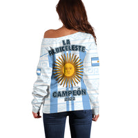 Suéter off-shoulder celeste con “VAMOS ARGENTINA” y motivo AFA en el pecho