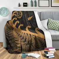 Dark blanket with gold koru and fern motifs, with white edge trim on sofa