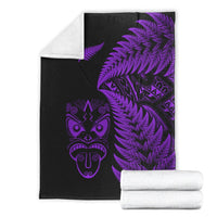 Folded black blanket with purple fern and Maori face design, plus white backing edge