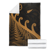 Dark gold-patterned blanket with white backing corner; rolled white throw beside it