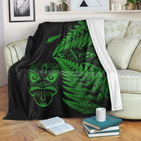 Black blanket with green fern leaves and Maori face design, white trim along edge