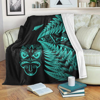 Black fleece blanket with turquoise fern fronds and Maori mask graphic on one side