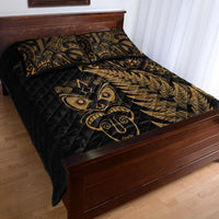 Black quilted bedspread corner with gold fern print and tribal mask emblem; 1 pillow shown