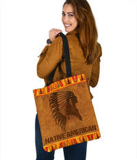 Brown tote bag showing side panel headdress artwork and orange tribal trim, black strap handles