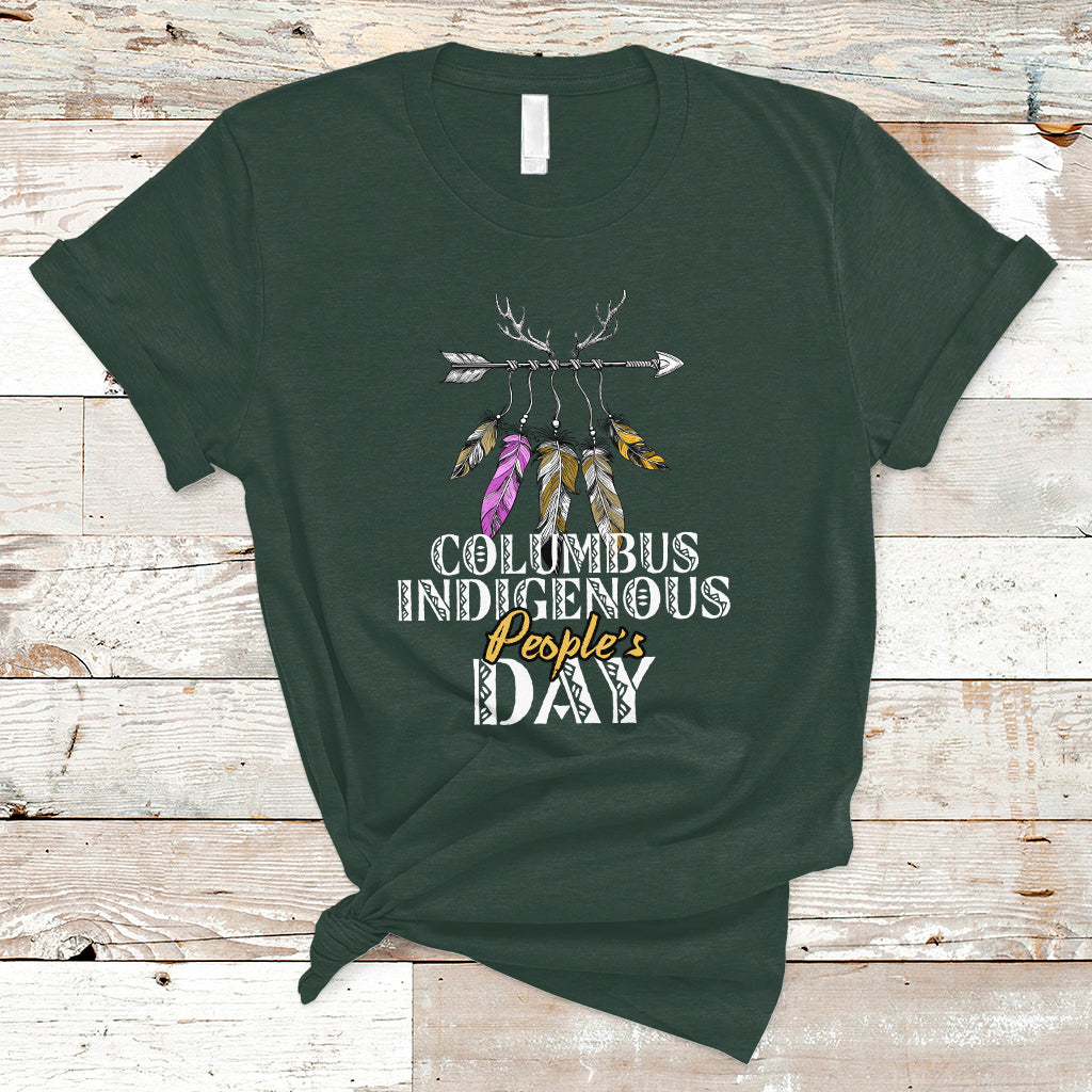 Dark forest green T-shirt with colorful feather arrow graphic and “Columbus Indigenous People’s Day” text