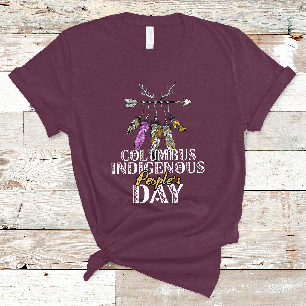 Maroon T-shirt with colorful feather arrow graphic and “Columbus Indigenous People’s Day” text