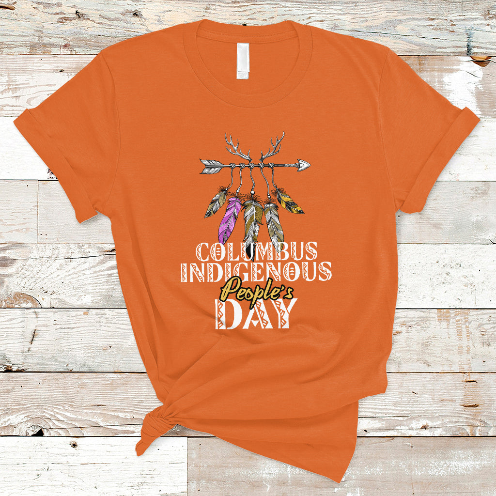 Orange T-shirt with colorful feather arrow graphic and “Columbus Indigenous People’s Day” text