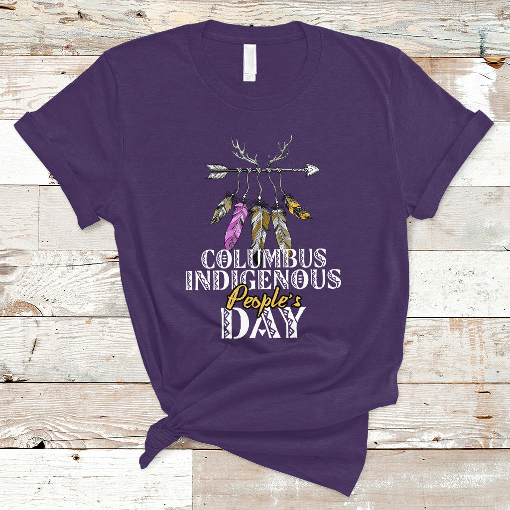 Purple T-shirt with colorful feather arrow graphic and “Columbus Indigenous People’s Day” text