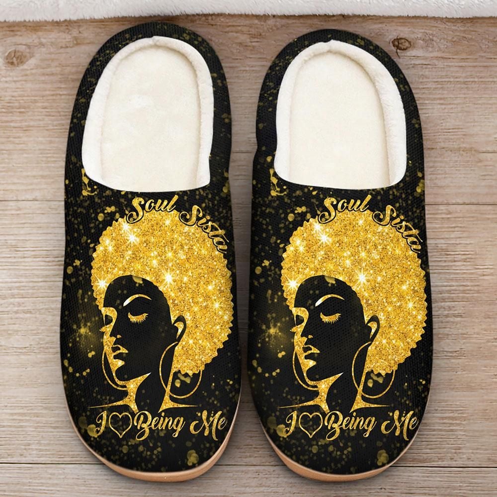 Black fleece slip-on slippers with gold graphic face and “Being Me” text
