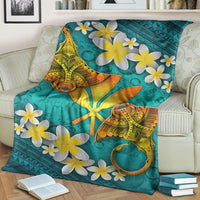 Turquoise Hawaiian blanket with manta ray graphic and scattered white-and-yellow plumeria blooms