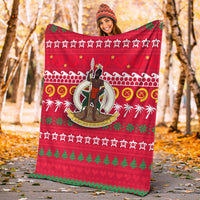Red Christmas blanket held up outdoors, with central warrior emblem and green holiday patterns