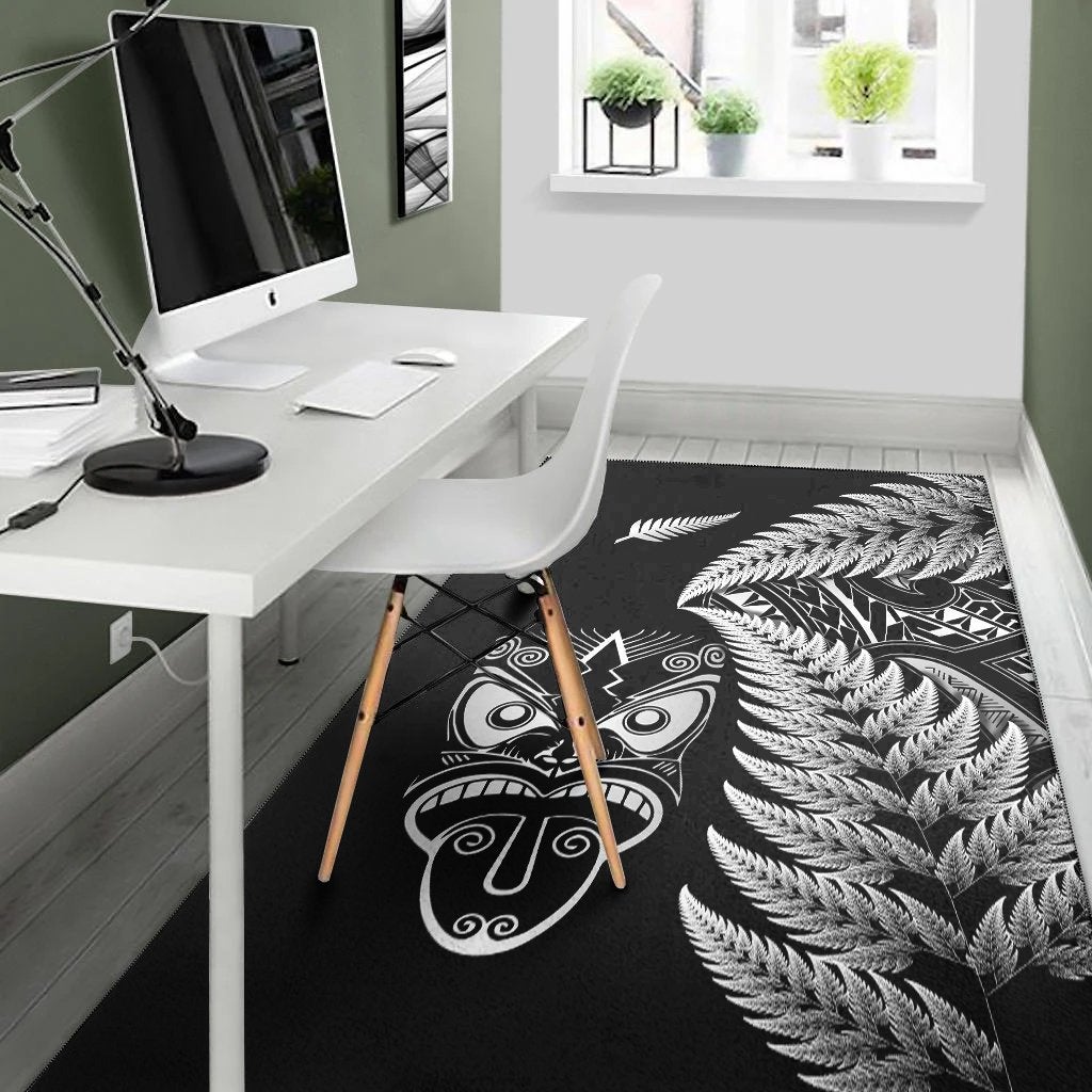 Black rug with white Maori mask and sweeping fern fronds, shown in workspace
