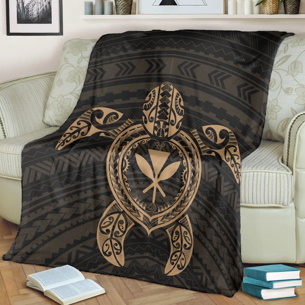 Black blanket draped on sofa, featuring gold turtle emblem and geometric stripe pattern