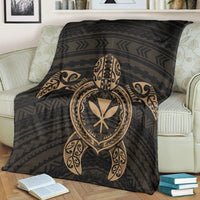 Black blanket draped on sofa, featuring gold turtle emblem and geometric stripe pattern