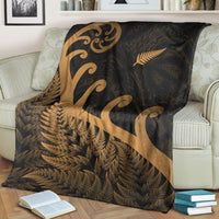 Dark blanket with gold koru swirl and fern motifs, draped over sofa cushions