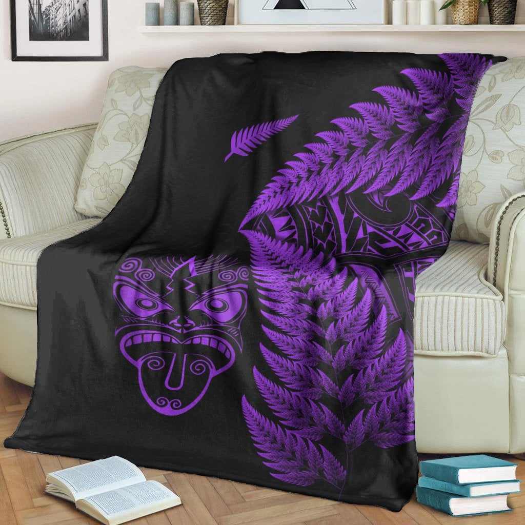 Black fleece blanket draped on couch with purple fern fronds and Maori mask graphic