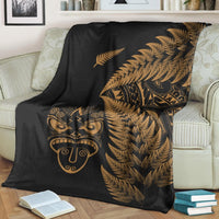 Black throw blanket with gold fern fronds and Maori mask print, draped over sofa