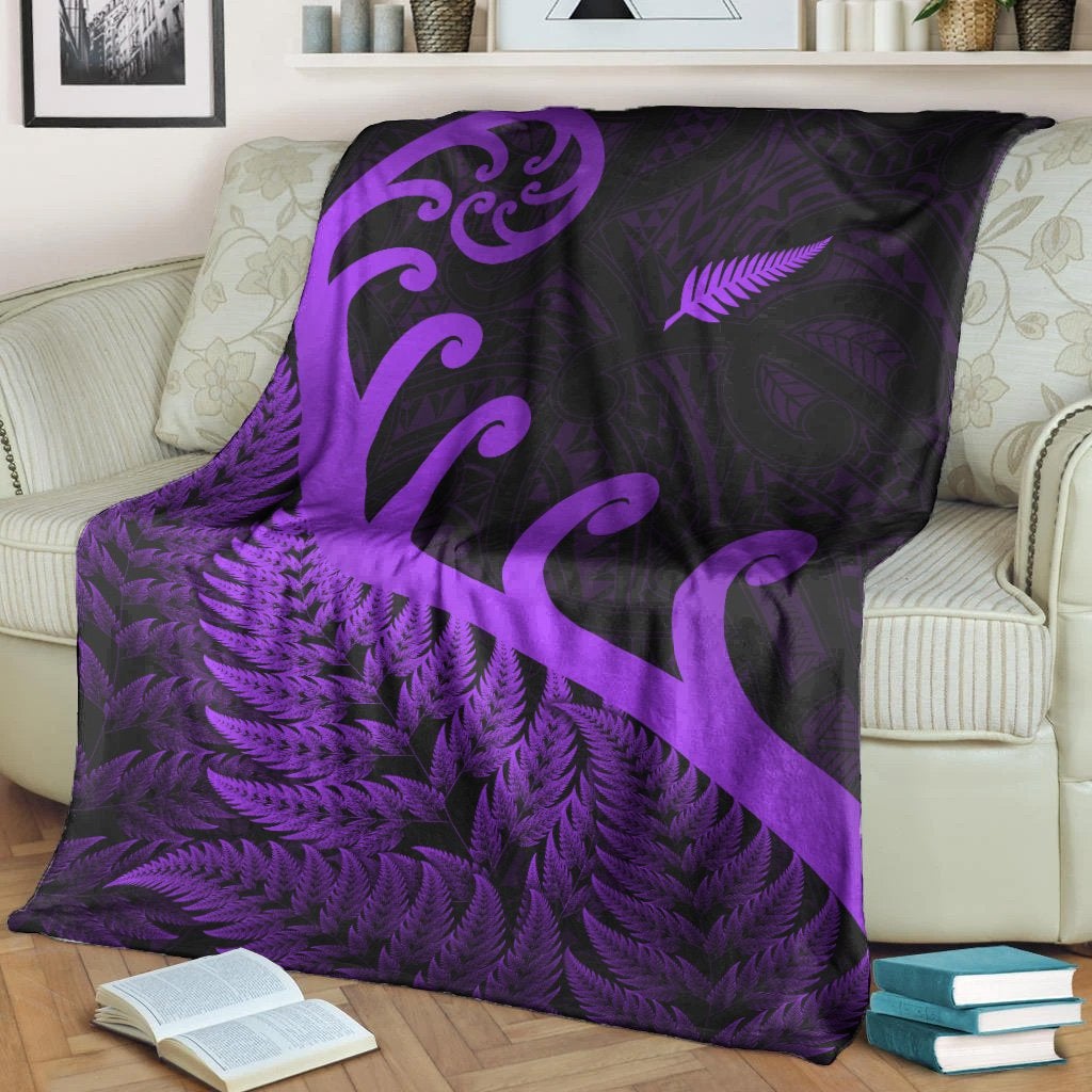 Purple and black throw blanket on couch with fern leaves, koru swirls, white border.