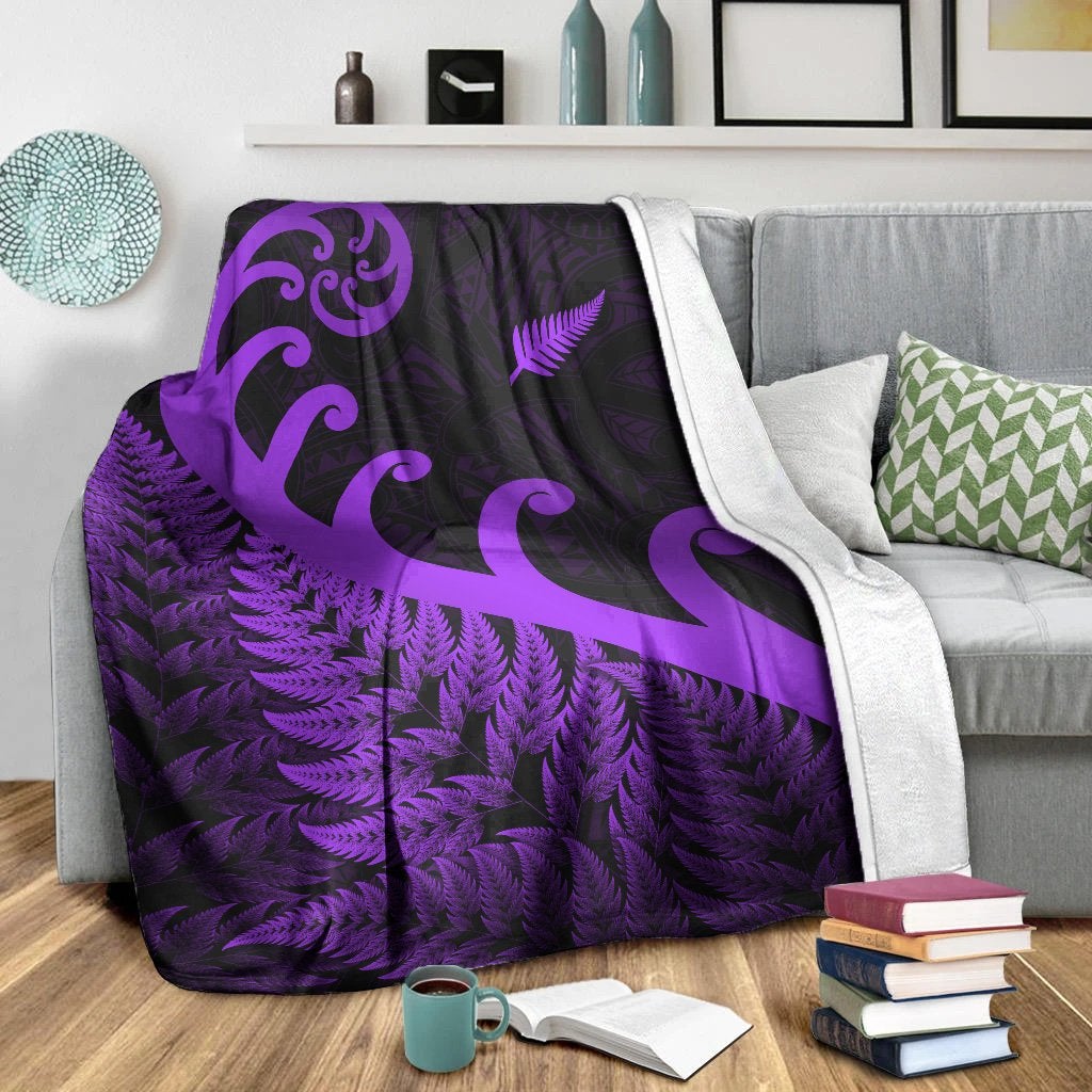 Purple and black blanket draped over sofa with fern texture and large koru motifs.