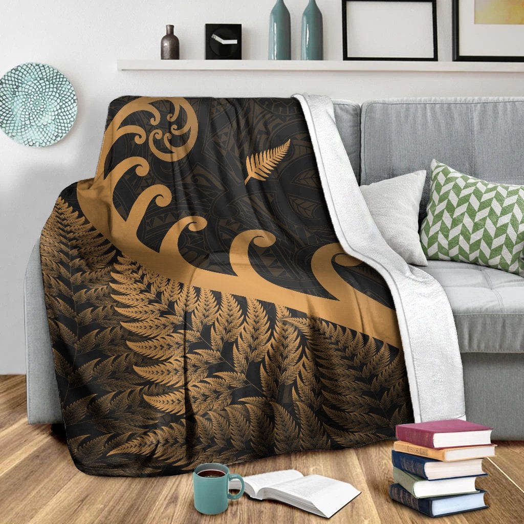 Dark blanket with gold koru and fern motifs, with white edge trim on sofa