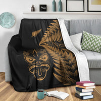 Black blanket with gold fern and Maori face graphic plus white edge trim, on couch
