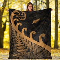 Large dark blanket with gold koru swirl and fern design, held open outdoors