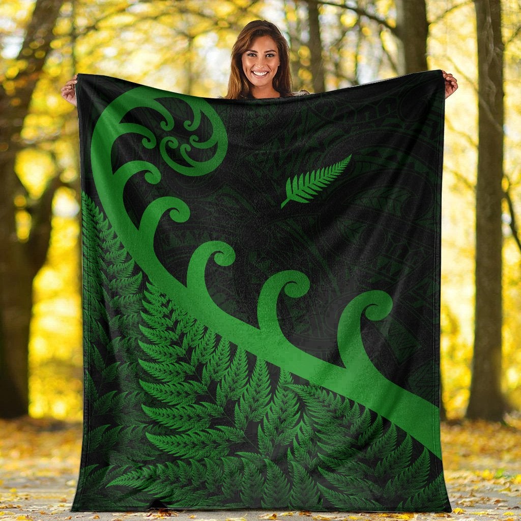 Green and dark green blanket with koru swirls and fern pattern held outdoors