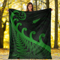 Green and dark green blanket with koru swirls and fern pattern held outdoors