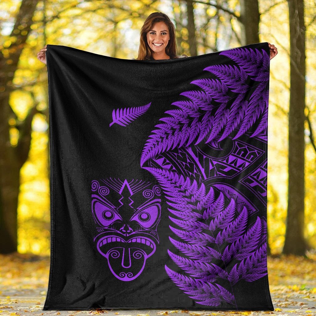 Black and purple Maori blanket with fern fronds and mask graphic, shown held up outdoors