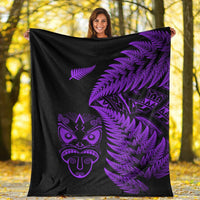 Black and purple Maori blanket with fern fronds and mask graphic, shown held up outdoors