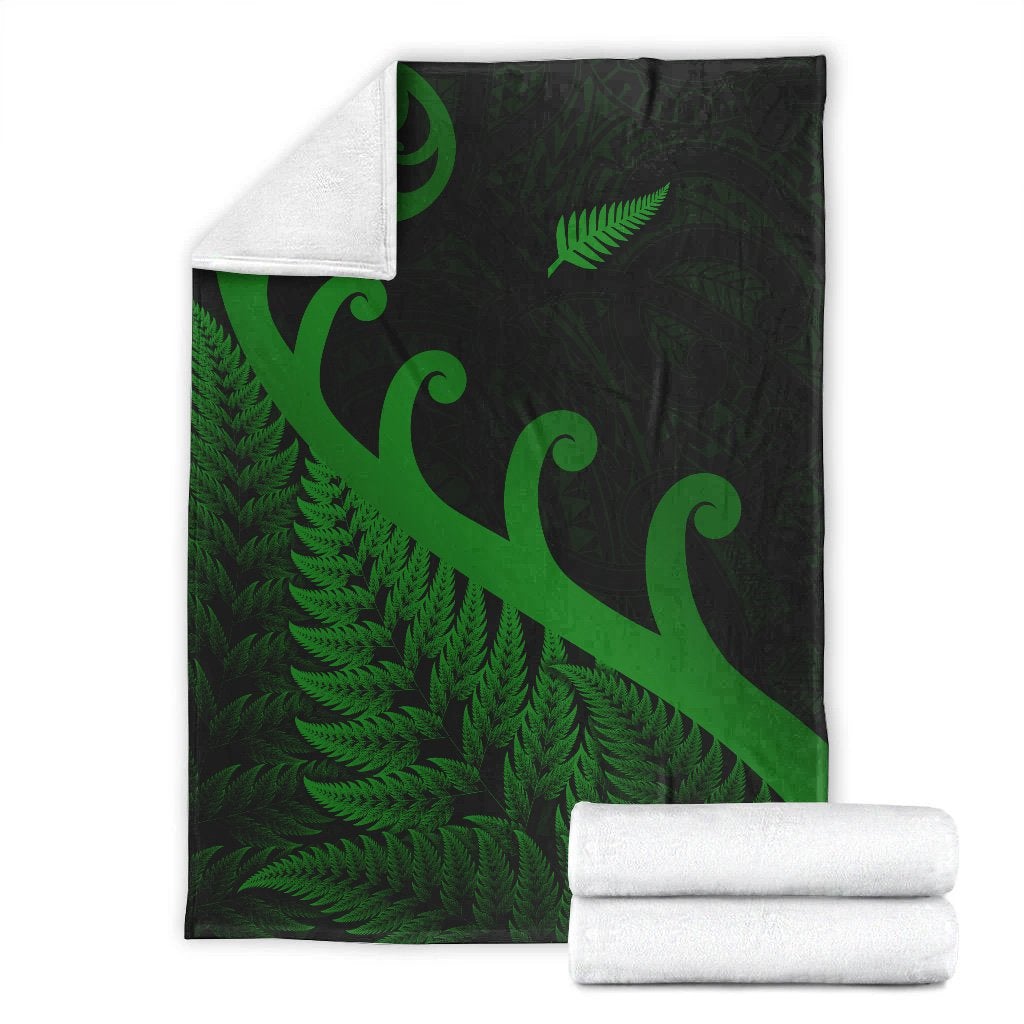 Folded green and dark green blanket with koru swirls and fern pattern, plus rolled towels