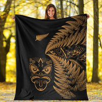 Black blanket held outdoors, featuring gold fern leaves and Maori face emblem