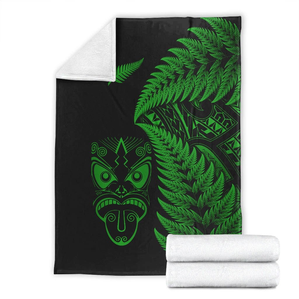Folded black blanket with green fern and Maori face print; white rolled blanket