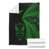 Folded black blanket with green fern and Maori face print; white rolled blanket