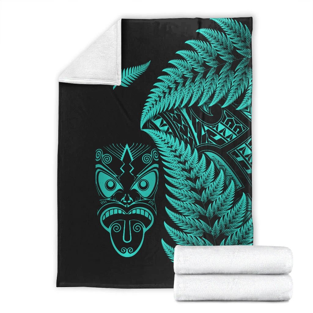 Black blanket with turquoise fern and Maori mask print, folded with rolled white lining