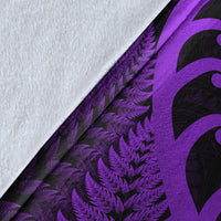 Close-up of blanket fabric: white reverse side with purple fern print and dark koru shapes.