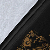 Close-up of black fabric blanket with gold fern and Maori face motif detail