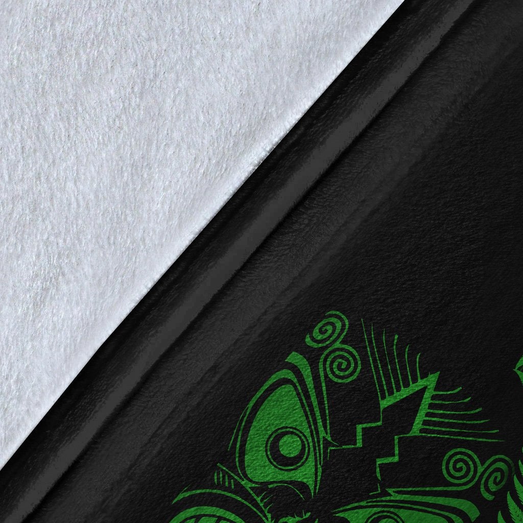 Close-up of black blanket fabric with green Maori face and fern pattern, textured weave