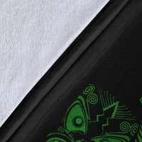 Close-up of black blanket fabric with green Maori face and fern pattern, textured weave