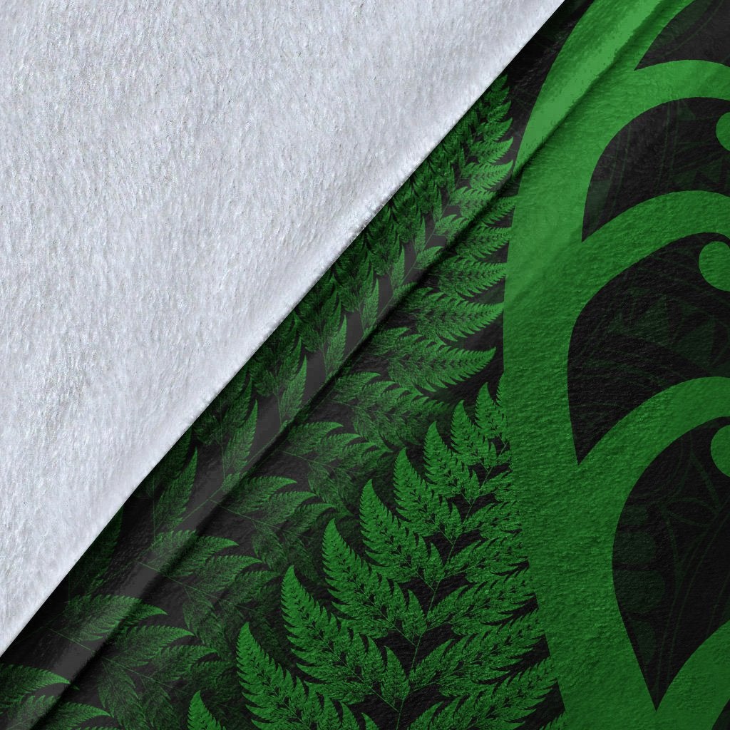 Close-up of green fern and koru print on dark blanket fabric with white backing edge
