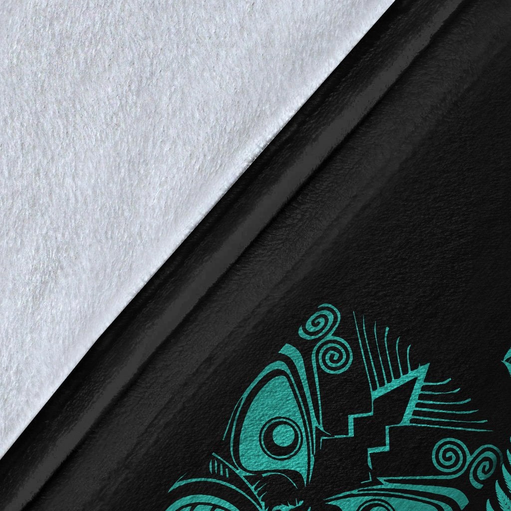 Close-up of black blanket fabric with turquoise Maori symbol and fern frond print
