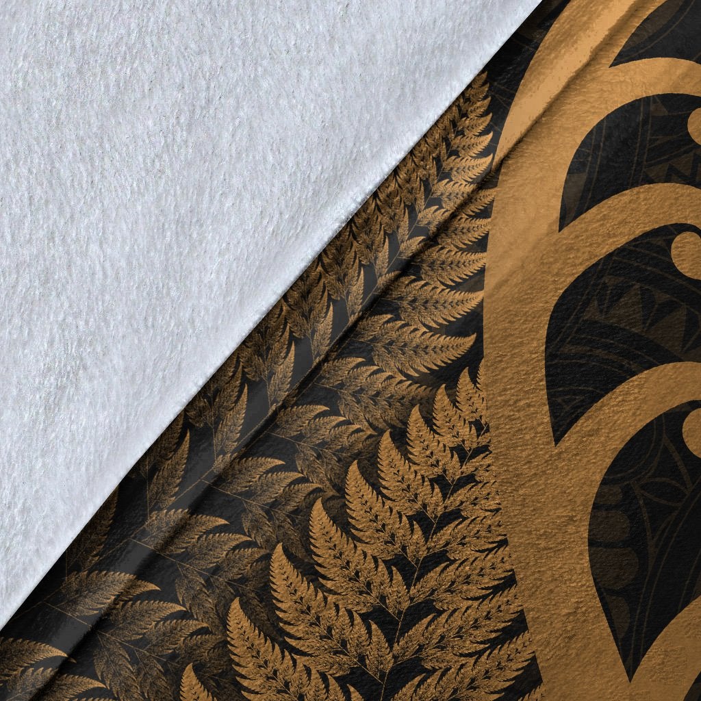 Close-up of blanket edge: white backing with gold fern and koru print on dark fabric