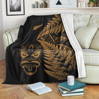 Black fleece blanket with gold fern pattern and Maori face design, folded with white border